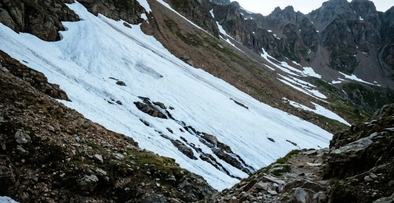 Steiles Altschneefeld auf schattigem Nordhang eines alpinen Wanderwegs im Frühsommer mit teilweise schneefreien Bereichen
