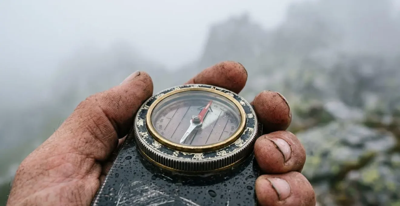 Hand hält Kompass zur Orientierung im dichten Nebel auf einem Bergweg