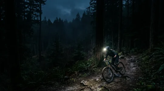Mountainbiker mit heller Helmlampe auf dunklem Waldtrail bei Nacht