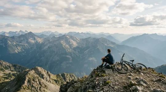 Mountainbiker macht Pause auf einem Berggipfel mit weitem Alpenpanorama im Hintergrund