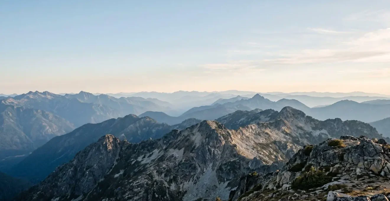 Weiter Blick über mehrere Alpengipfel-Schichten im sanften Morgenlicht mit endlosem Horizont